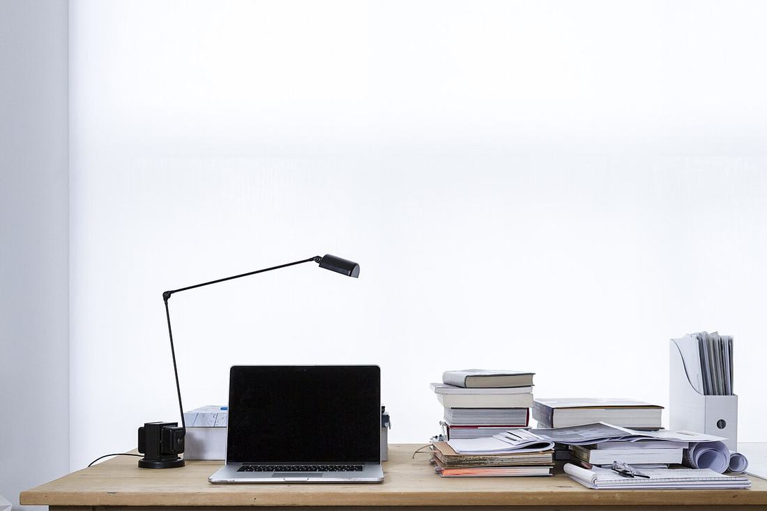 A laptop on a desk beside stacks of books